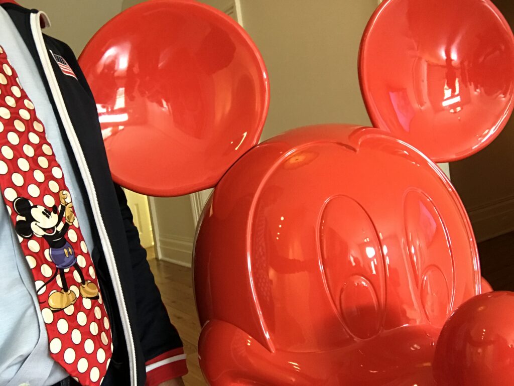 Red Mickey Mouse head next to man wearing Mickey Mouse tie