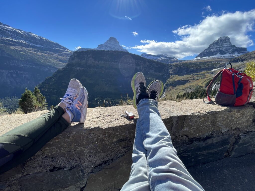 Two sets of feet propped up on rock barrier in mountains